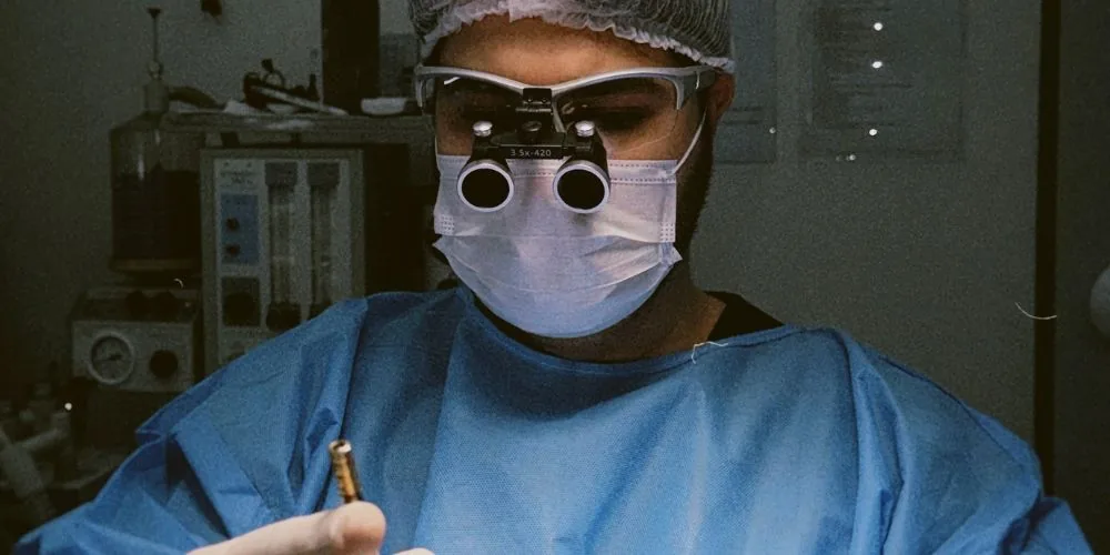 Dr. Éric Aguiar com lupa cirúrgica durante procedimento de transplante capilar FUE
